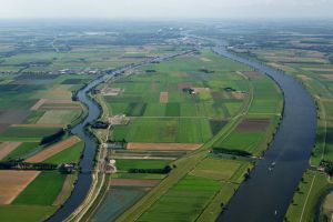 Luchtfoto van een brede rivier die door groen akkerland kronkelt, met een vrachtschip erop.