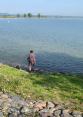 Jongere man met rugzak staat aan waterkant, kijkt naar meer.