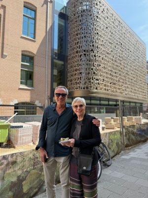Man en vrouw glimlachen, vrouw houdt notitieboekje vast, gebouw met tekst.