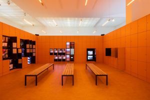 Oranje lockers en houten banken in een modern museum met displaykasten met documenten.