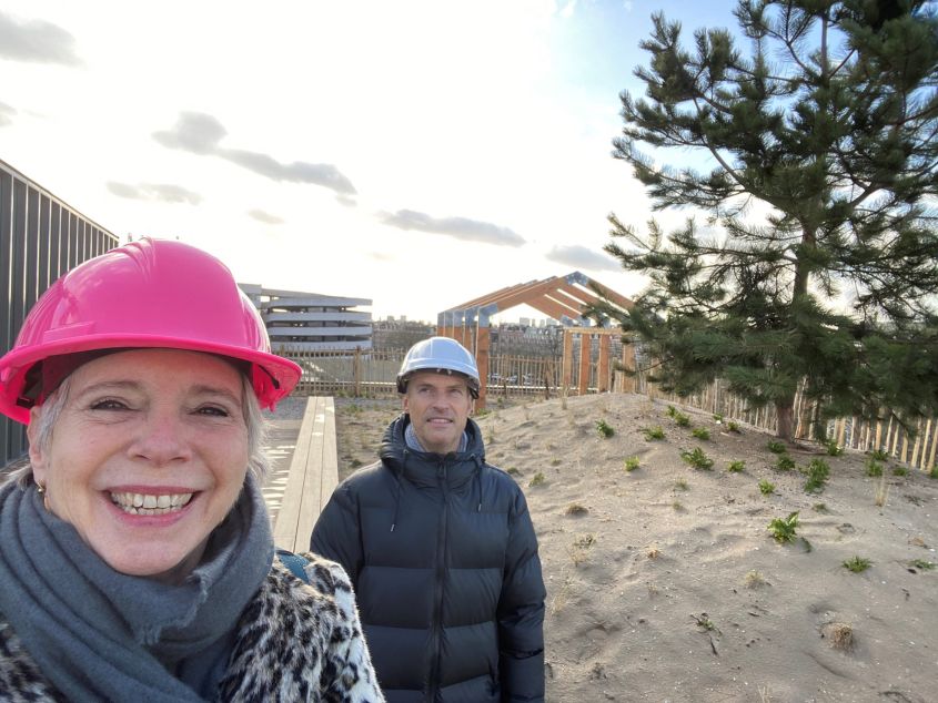 Twee personen met bouwhelmen bij een houten constructie in het zand.