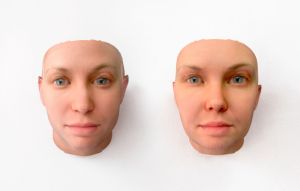 Twee levensechte, 3D-geprinte, kale gezichten met blauwe ogen en roze huid, naast elkaar op een witte achtergrond.