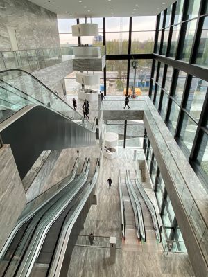 Moderne lobby met marmeren muren, glazen balustrades en roltrappen. G- en K-borden zichtbaar.