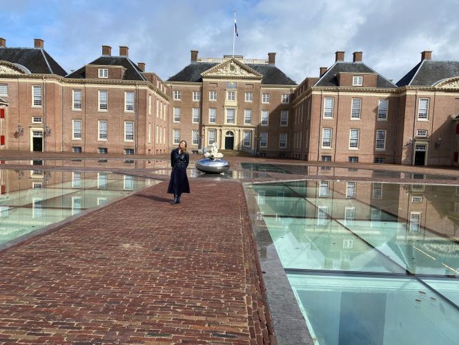 Vrouw bij het museum Paleis Noordeinde met reflecterend plein en monument.