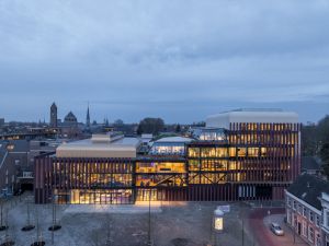Modern gebouw met veel glas en baksteen, verlicht in de schemering.