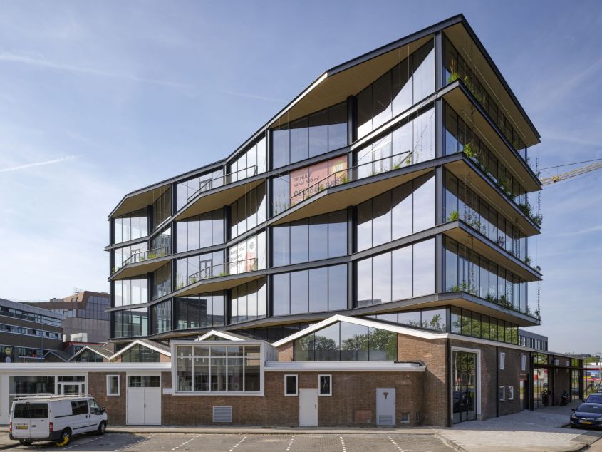 Modern kantoorgebouw met glazen gevels en uitstekende balkons. Oranje poster met tekst 'TE HUUR'.