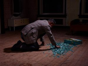 Man in geruite jas knielt op de vloer, maakt een puzzel, naast een puzzeldoos met de tekst "4000".