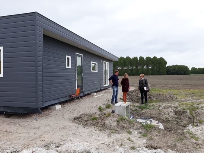 Modern grijs huis met drie personen ernaast, bouwterrein met greppel en pijpen