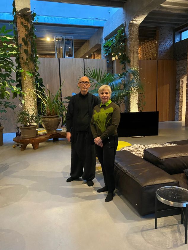 Man en vrouw poseren in een stijlvolle woonkamer met veel planten en meubels.