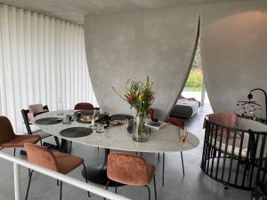 Eettafel met stoelen en bloemen, met babybedje en meubels op de achtergrond.
