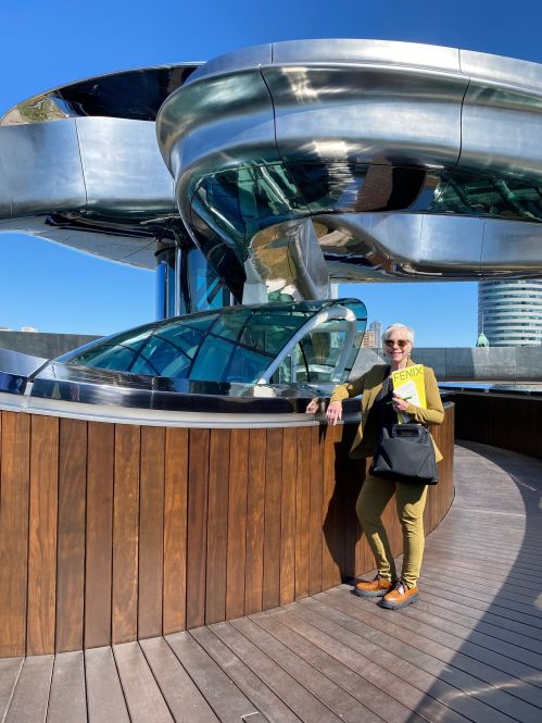 Vrouw met gele map met tekst FENIX staat op houten terras voor modern gebouw