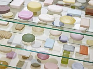 Veel verschillende soorten zeep in diverse kleuren en vormen, tentoongesteld op glazen planken.