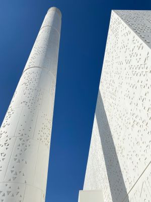 Witte cilinder en rechthoekig gebouw met geometrische patronen, tegen een helderblauwe lucht.