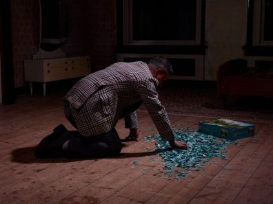 Man in geruite jas knielt op de vloer, maakt een puzzel, naast een puzzeldoos met de tekst "4000".
