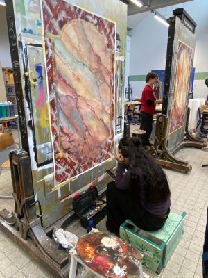 Kunstenaars schilderen in een atelier, grote schilderijen op ezel, paletten en gereedschap zichtbaar.