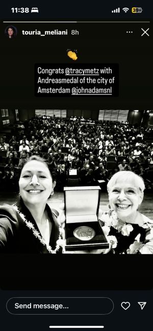Twee vrouwen tijdens de uitreiking van de Andreas penning, met medaille en bloemenkrans op podium.