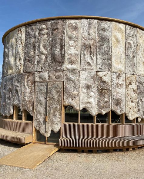 Ronde, stenen structuur met houten zitbanken en toegangshelling.
