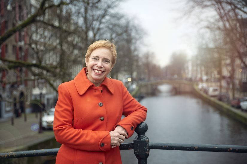 Vrouw met oranje jas lacht op brug in Amsterdam met gracht op achtergrond