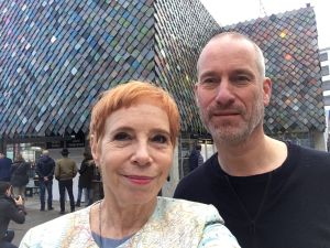 Twee mensen voor gebouw met schubachtige gevel; tekst op gebouw: "People's Pavilion" en "World Design Event".