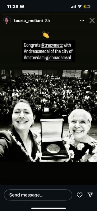 Twee vrouwen tijdens de uitreiking van de Andreas penning, met medaille en bloemenkrans op podium.