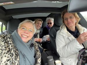 Vier vrouwen in een auto met schuifdak genieten van hapjes op een regenachtige dag.
