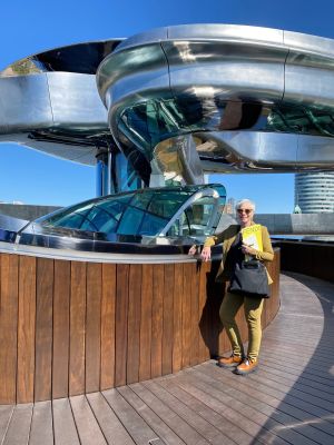 Vrouw met gele map met tekst FENIX staat op houten terras voor modern gebouw