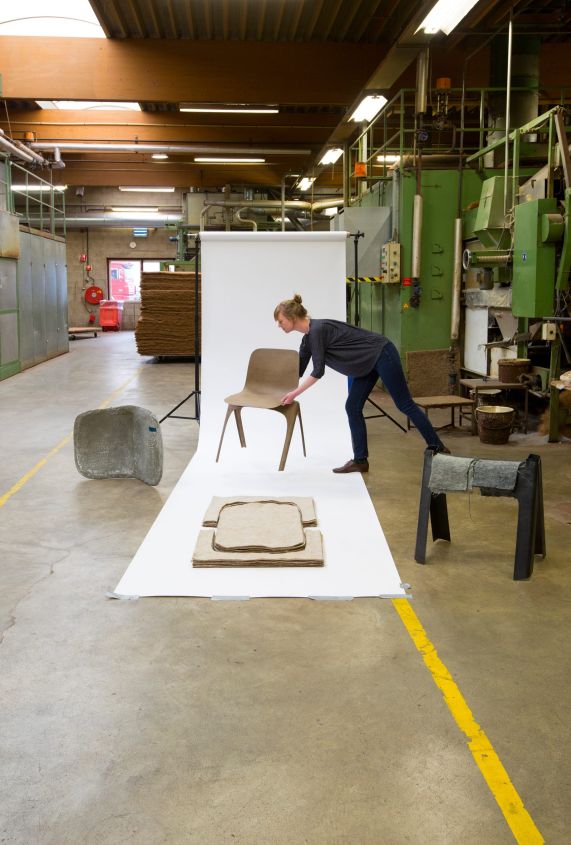 Vrouw plaatst bruine stoel op witte achtergrond in fabriek.