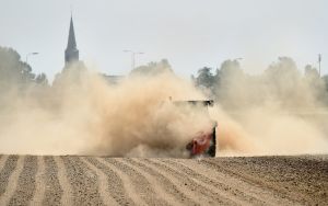 Oranje tractor met veel stof in de lucht, ploegt een veld met rijen.