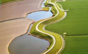 Bochtige waterwegen omgeven door groene en bruine akkers.