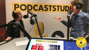 Podcaststudio met twee mensen met koptelefoons, microfoons, en een laptop met "PODCASTSTUDIO" erop.