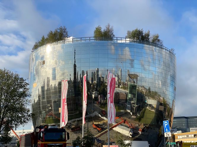 Grote glazen, ronde gebouw met bomen op het dak. Vlaggen met "Het Nieuwe Instituut".