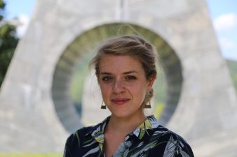Vrouw met blond haar, met geometrische oorbellen, staat voor een kunstwerk met een rond gat.