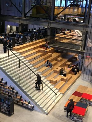 Een bibliotheek met houten trappen, zitplekken, boekenplanken en mensen die studeren en boeken lezen.