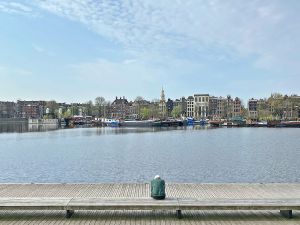 Persoon op bank kijkt uit over water naar Amsterdamse huizenrij met boten.